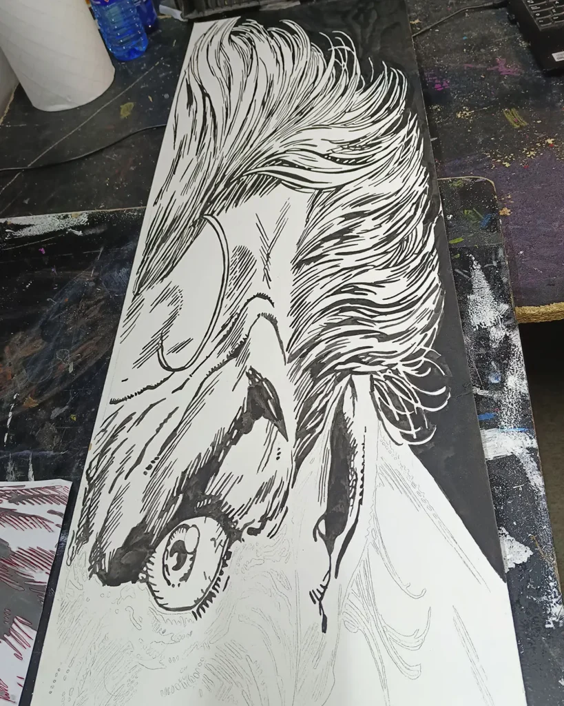 Proceso de ilustración en blanco y negro estilo cómic de personaje tipo Joker sobre mesa de trabajo en taller artístico.